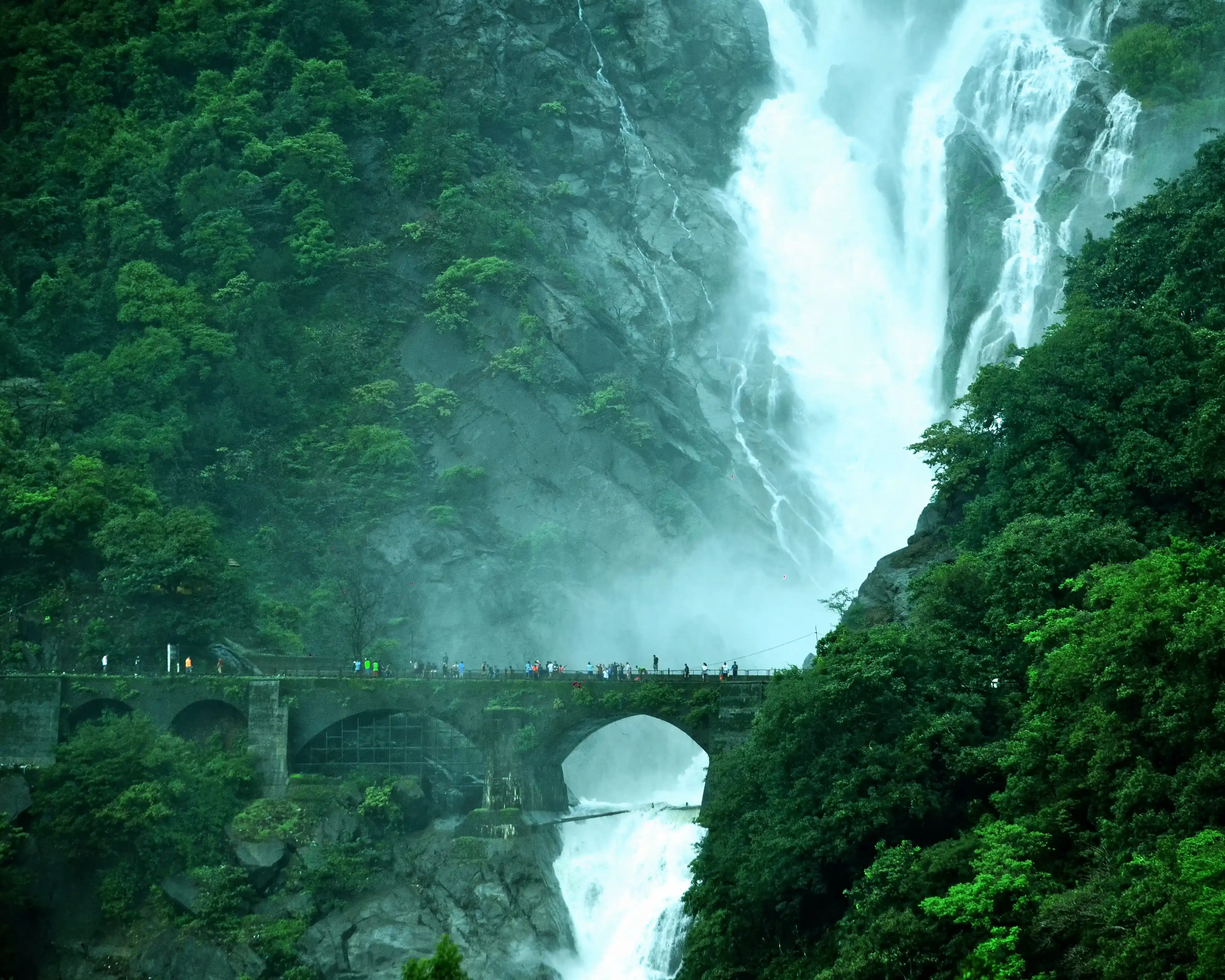 Trekkers standing at the base of the Dudhsagar cascade with white water plunging behind them